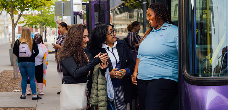 Passengers boarding a DART bus at a street stop, with two women conversing near the door on a sunny day