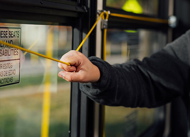A person pulling the yellow stop request cord on a bus near a reserved seating sign for passengers with disabilities