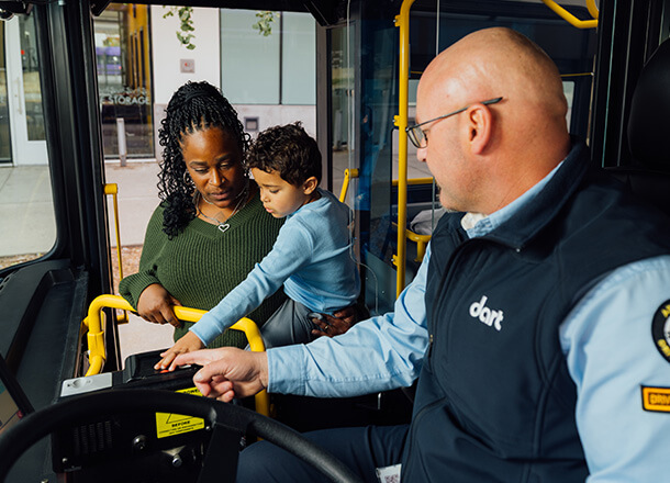 A DART staff member assisting a woman and young child with the fare payment machine while boarding the bus